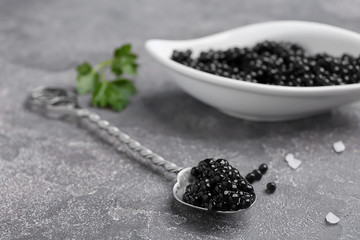 Fototapeta na wymiar Spoon and bowl with delicious black caviar on grey background