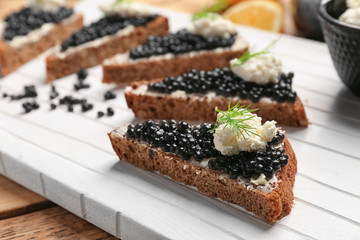 Sandwiches with delicious black caviar and cottage cheese on wooden board