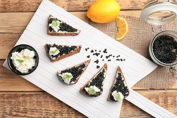 Sandwiches with delicious black caviar and cottage cheese on wooden board