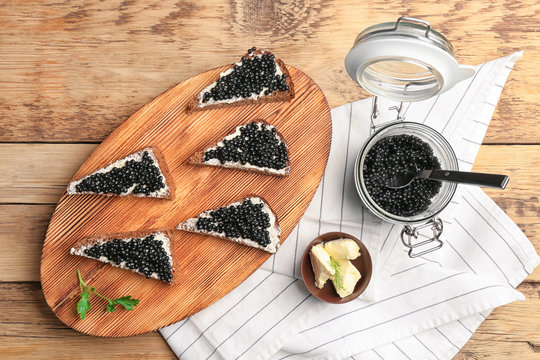 Sandwiches with delicious black caviar on wooden board