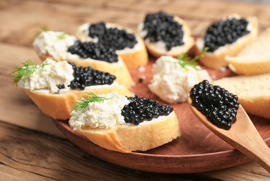 Sandwiches with delicious black caviar and cottage cheese on wooden plate