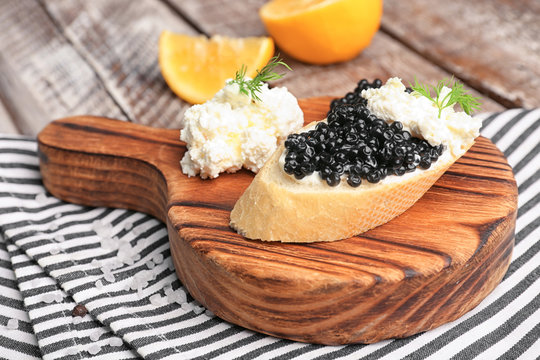 Sandwich with delicious black caviar and cottage cheese on wooden board