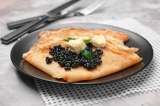 Thin pancakes with delicious black caviar and butter on plate