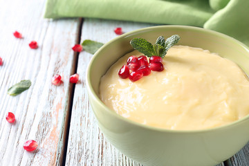 Tasty vanilla pudding with pomegranate seeds in bowl on table