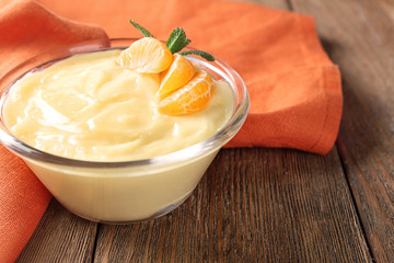 Tasty vanilla pudding with tangerine in bowl on table