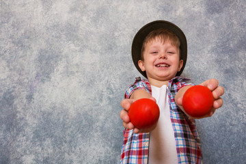 Fototapeta na wymiar A funny little boy dressed in red checkered shirt and an old fashioned hat, holding hands red Easter eggs. Copy space.