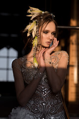 Portrait of a beautiful girl with flowers in her hair. Dress with rhinestones. Hands at the face. Light from the sun on the face. Looking sideways.