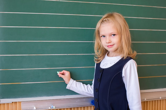 First grade pupil a girl writing on green blackboard at school lesson