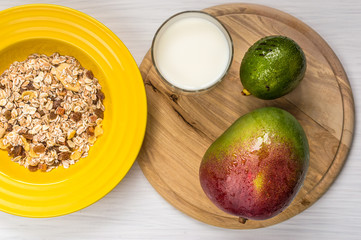 fruit, muesli and milk for breakfast. yellow plate, wooden board, white background.