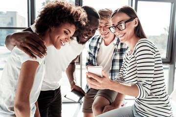 Innovative technology. Happy positive young woman holding her smartphone and showing in to her colleagues while interacting with them