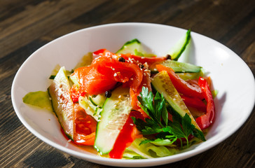 Salad with smoked salmon and cucumber, tomato, pepper in bowl on a wooden background