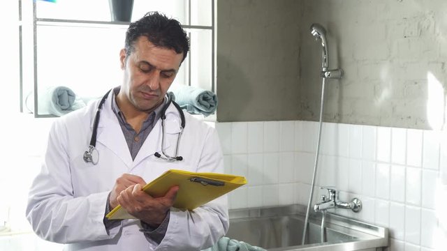 Handsome mature Hispanic male professional veterinarian doing paperwork at his clinic smiling to the camera profesion occupation doctor medicine healthcare job practitioner specialist care.