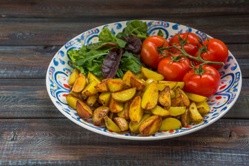 Fried baby potatoes, green salad and fresh tomatoes on a big plate in rustic style