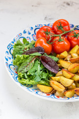 Fried baby potatoes, green salad and fresh tomatoes on a big plate in rustic style