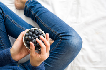 Healthy eating concept. Woman having blueberries in bed. Top view.