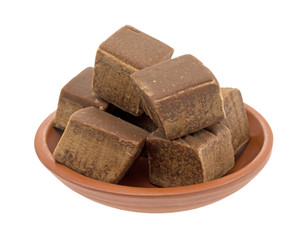 Several chunks of butter chocolate fudge in a small red clay bowl isolated on a white background.