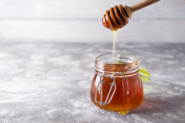 Spoon of honey with jar on a light background