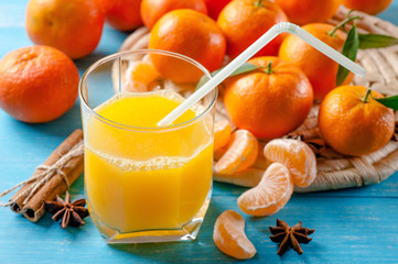 Glass of fresh orange juice, tangerines and cinnamon on wooden background