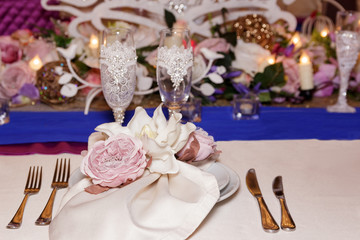 A wedding decor of white dishes, white bouquets with flowers, candles and glasses stand on a light tablecloth of a served table in a restaurant. Side view, selective focus