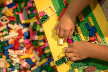 Close up of child's hands playing with colorful plastic bricks at the table. Early learning. stripe background. Developing toys