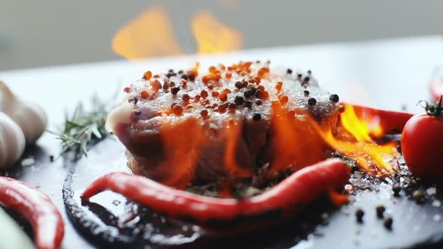close-up view of raw uncooked slice of meat and fresh vegetables with flames. bbq burn original mexico recipe dish black plate chilli pepper professional cooking exotic meal cook recipe preparing food