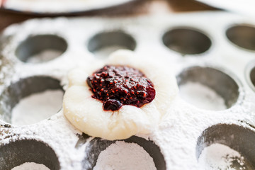 Piece of mochi sticky glutinous rice cake dusted with starch flour to make dessert in muffin pan tin, with raspberry jam filling