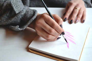 Naklejka premium Woman paints in a sketchbook. Tools for painting on the white wooden desk. Painter work.