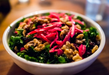 Macro closeup of kale red pepper beet shredded green vegan vegetarian salad in restaurant with candied nuts, walnuts, on wooden table in evening dinner