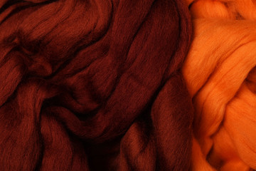 Bright colored merino wool for felting and needlework, hobby. The stripes of burgundy color and orange yarn folded into abstract pattern. Abstract art background