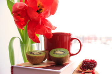Obraz na płótnie Canvas Healthy lifestyle. Red flat lay: fresh fruits kiwi, pomegranate. Red tulips and cup on the book.