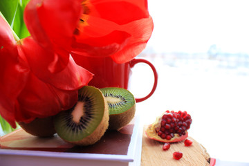 Healthy lifestyle. Red flat lay: fresh fruits kiwi, pomegranate. Red tulips and cup on the book.