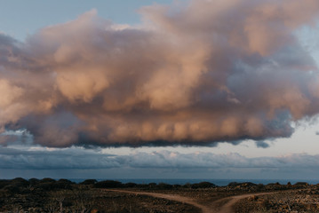 Huge gold clouds above the ocean and two hiking trails on the front on the sunrise. Tenerife 