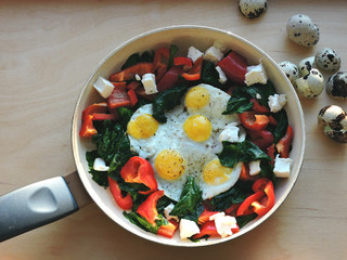 Appetizing fried quail eggs with spinach, feta cheese and peppers.