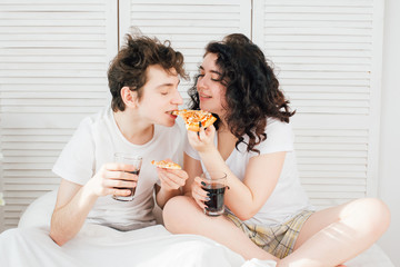 Couple watching TV in bed and eating pizza