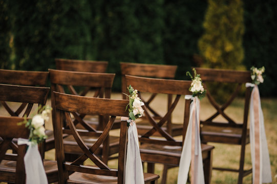Very beautiful outside ceremony. classical wedding in forest. The arch is wooden. White flowers. Brown chairs. Rite. Bride and groom. Decor. Floristics. In the open air. Path from the petals of roses.
