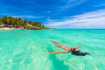 Naklejka premium Atrakcyjna młoda kobieta relaksuje w turkusowych wodach morze karaibskie przed raj plażą w Tulum, blisko Cancun, Riviera Maya, Meksyk