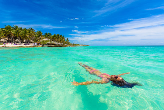 Attractive young woman relaxing in turquoise waters of Caribbean Sea in front of paradise beach in Tulum, close to Cancun, Riviera Maya, Mexico
