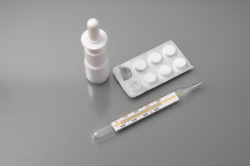 medical thermometer with tablets and a spray for the nose on a gray background in the studio.