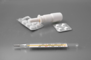 medical thermometer with tablets and a spray for the nose on a gray background in the studio.