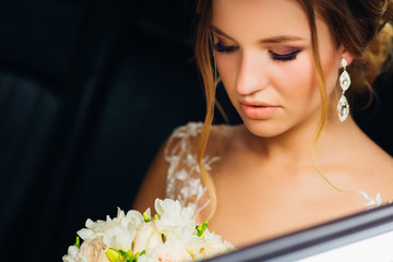 Obraz na płótnie Canvas A girl with a beautiful make-up sits in the car and looks at a beautiful bouquet of flowers