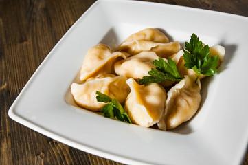 Meat dumplings - russian pelmeni, ravioli with meat on plate on a wooden background