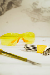 Repair carpenter tools: yellow screwdriver, wrench and protective glasses on white old wooden background, copy space