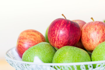 red apples on green apples in white wire basket