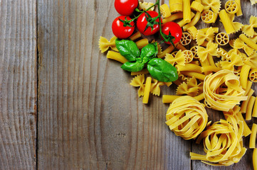 Tomato, basil and italian pasta rigatoni, fettuccine, penne, farfalle on wooden background
