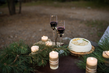 Two glass with red wine, wedding cake and a lot of candles decorated with pine branches. Romantic dinner for couple.  Wineglasses.