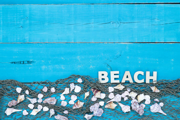 Blank rustic teal blue wood sign with seashells and fish netting border with the word BEACH; wooden background with copy space
