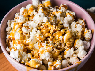 Popcorn with salted caramel in pink bowl on wooden board on dark background