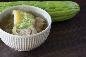 Stuffed bitter gourd with seasoned minced pork soup in ceramic bowl on brown wooden table Thai food
