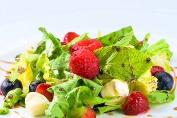 Appetizing fresh vegetarian salad with different berries, tomatoes, meat, basil leaves and sauce, close-up. For menu design