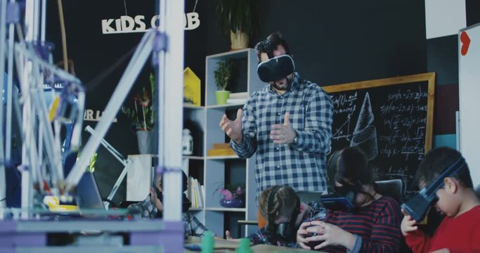 Teacher with group of children having class in school and studying VR technologies in goggles.